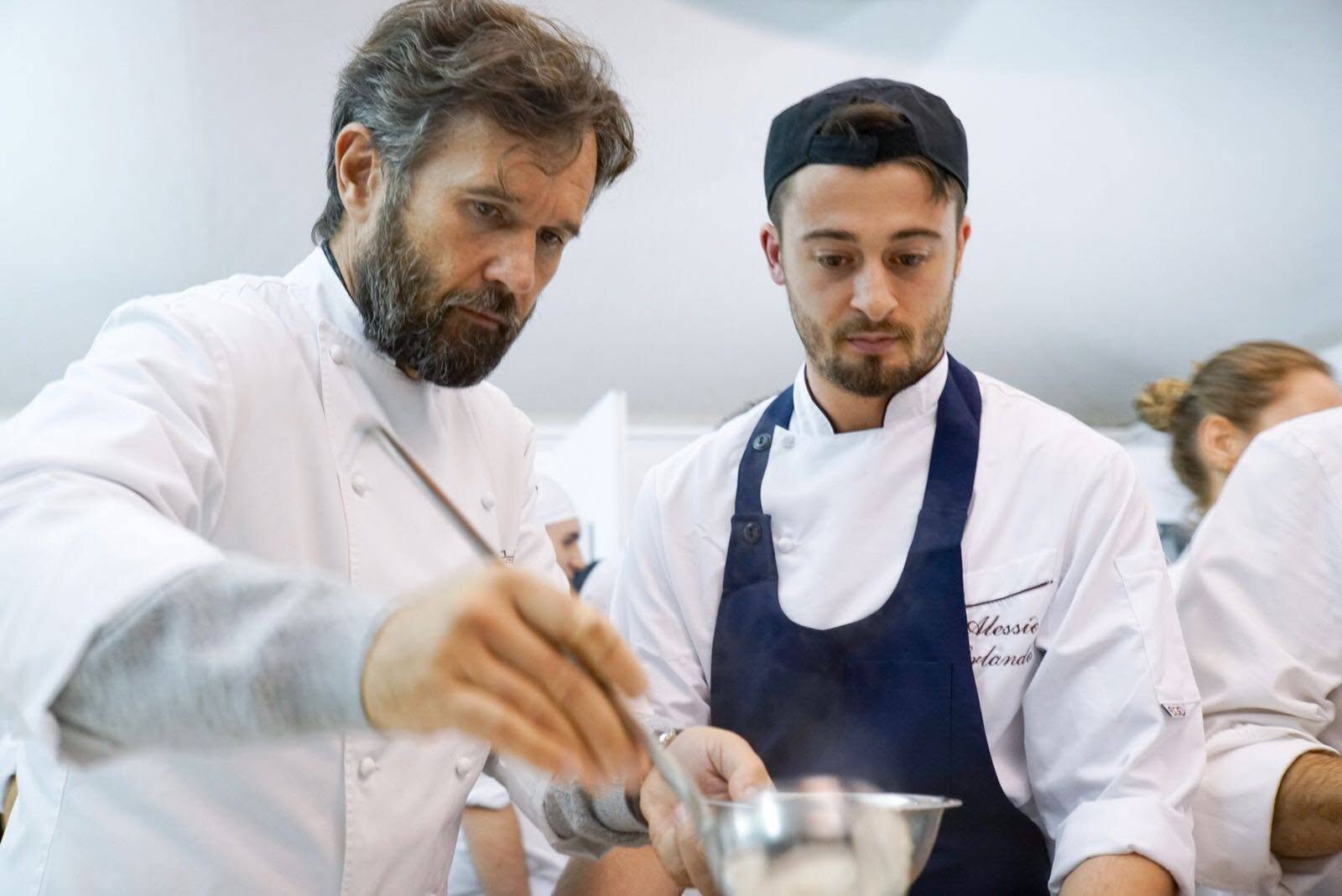 Uno chef affianca un giovane cuoco nella preparazione di un piatto