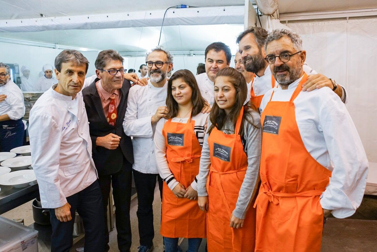 Un gruppo di chef stellati sorride insieme a due giovani con il grembiule arancione dell'evento