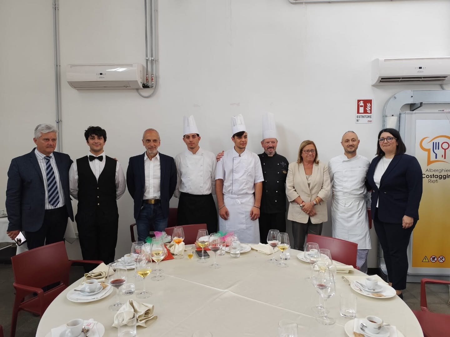 Foto di gruppo degli allievi di sala e cucina con lo staff didattico attorno a un tavolo apparecchiato
