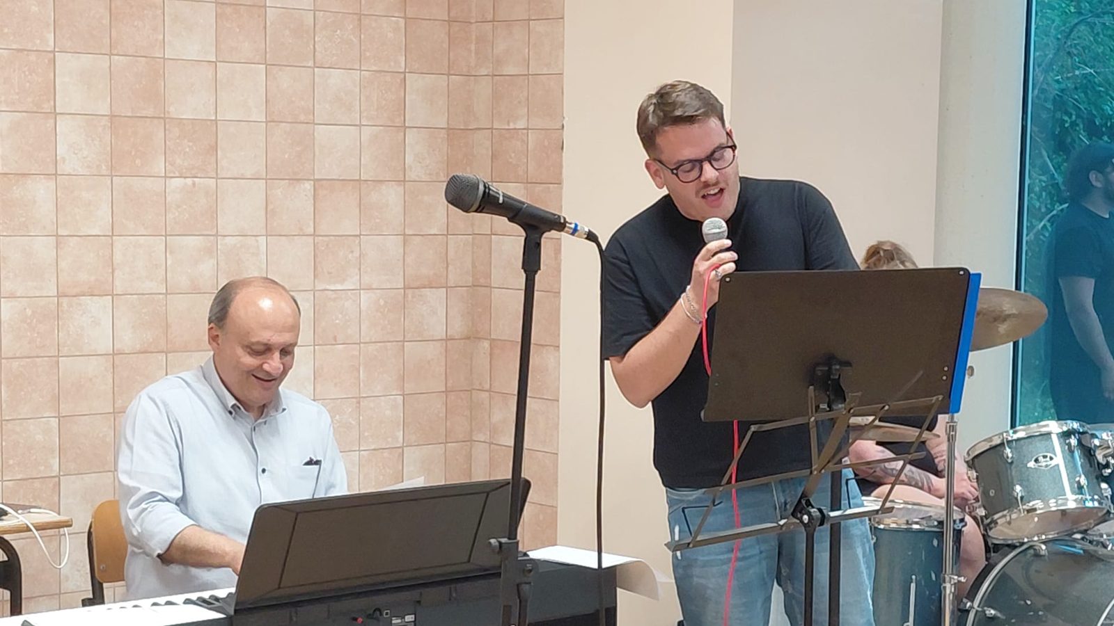 Un docente accompagna al pianoforte uno studente che canta